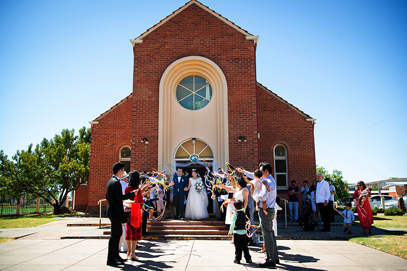 Couple walking out of the church in Adelaide with guests holding ribbons instead of confetti., Happy couple just married Adelaide wedding photography