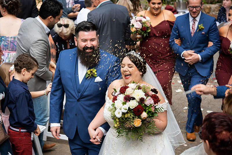 Couple walking down the aisle at Wood House Activity centre with guests throwing natural confetti, Happy couple just married wedding photography
