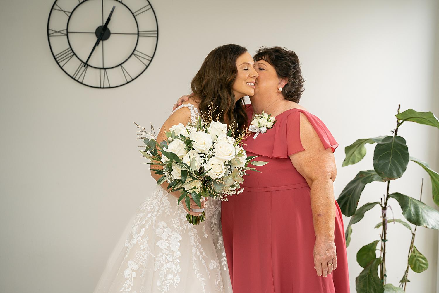 Bride and her mom during prep, bride kissing mom